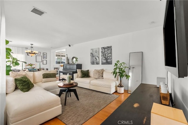 living area with light wood-type flooring, visible vents, and a chandelier