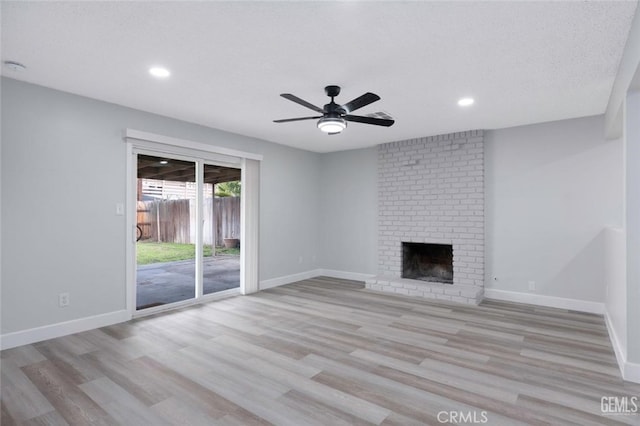 unfurnished living room featuring light wood-type flooring, a brick fireplace, ceiling fan, and baseboards