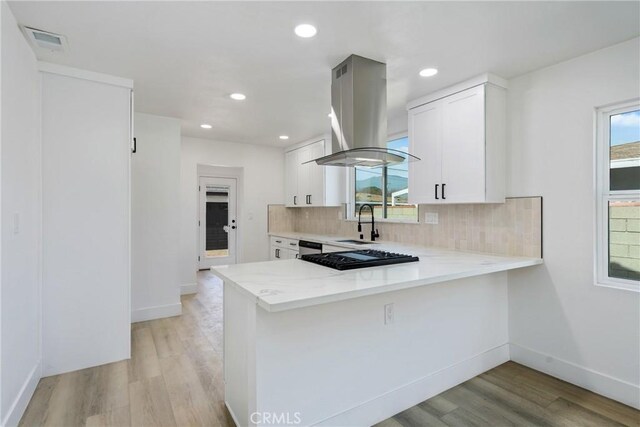 kitchen with island range hood, visible vents, decorative backsplash, a peninsula, and white cabinetry