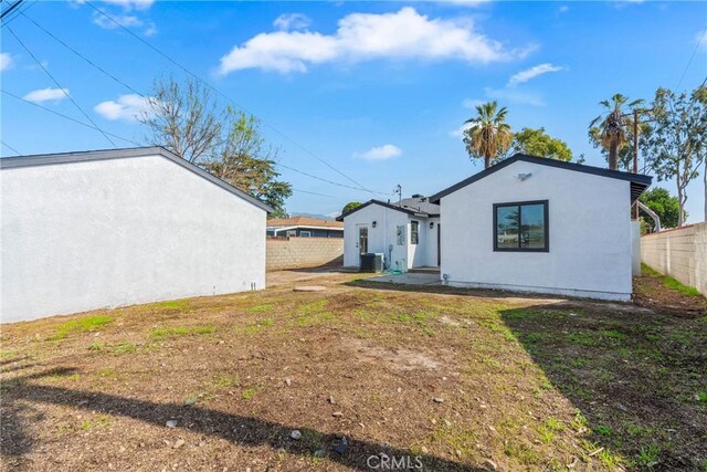 rear view of house featuring a yard, fence, and stucco siding