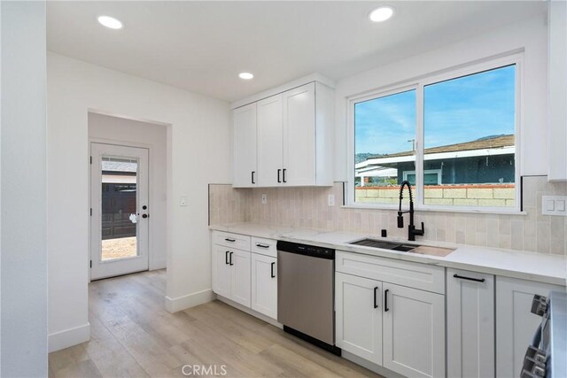 kitchen featuring light countertops, dishwasher, a sink, and white cabinetry