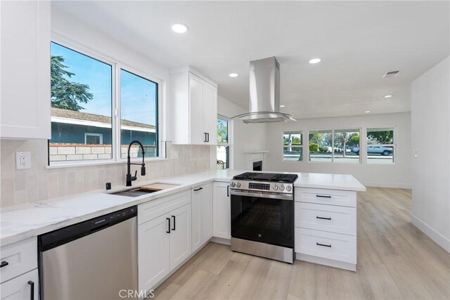 kitchen featuring a peninsula, a sink, white cabinetry, appliances with stainless steel finishes, and island exhaust hood