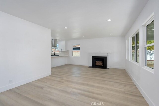 unfurnished living room with light wood-type flooring, a fireplace with flush hearth, baseboards, and recessed lighting