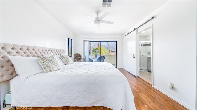 bedroom featuring access to exterior, visible vents, baseboards, a barn door, and wood finished floors