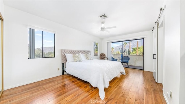 bedroom featuring light wood finished floors, visible vents, access to exterior, baseboards, and a barn door