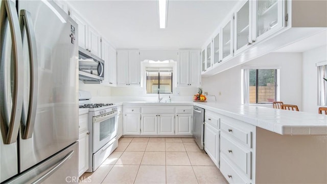 kitchen featuring a sink, white cabinetry, appliances with stainless steel finishes, a peninsula, and light tile patterned floors