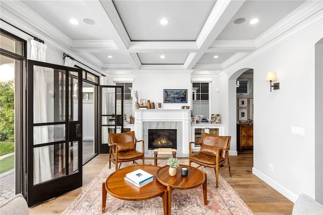 living area featuring beam ceiling, a fireplace, light wood-style floors, coffered ceiling, and baseboards