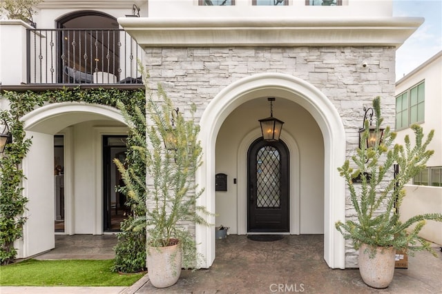 doorway to property featuring a balcony, stone siding, and stucco siding