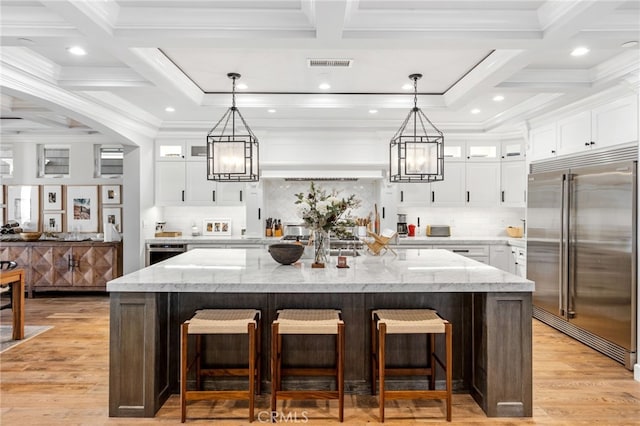 kitchen featuring a large island, built in fridge, glass insert cabinets, and white cabinets