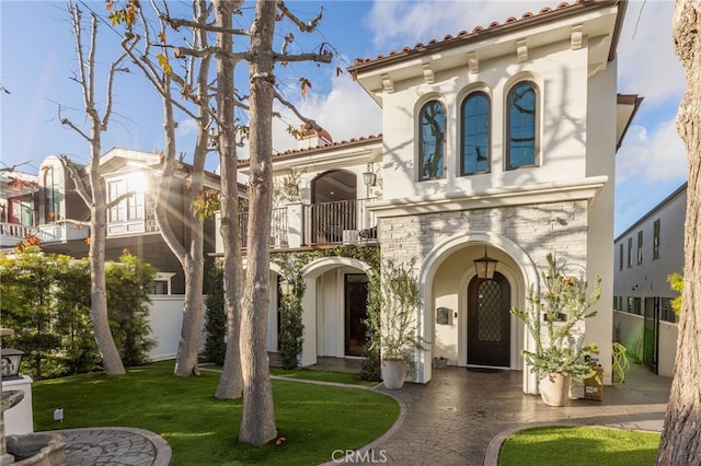 mediterranean / spanish-style home with a front yard, a tile roof, a balcony, and stucco siding