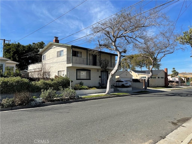 view of front of house featuring a residential view, a chimney, stucco siding, and a balcony