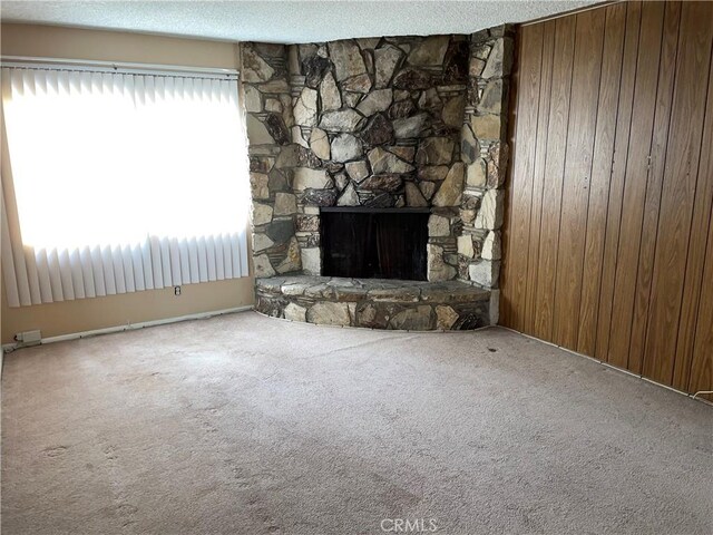 unfurnished living room featuring wooden walls, a textured ceiling, carpet floors, and a stone fireplace