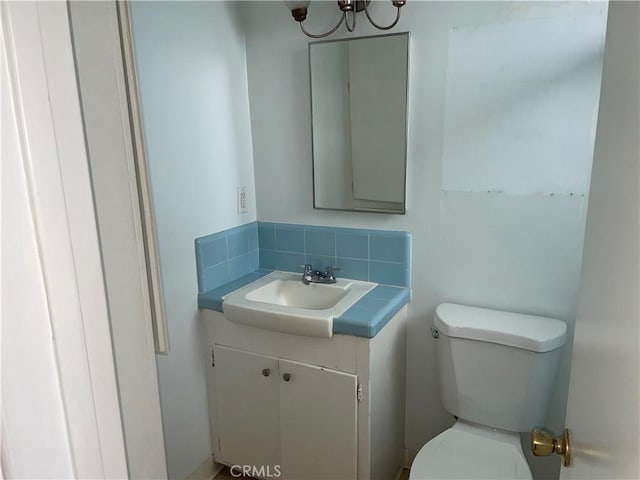 half bath with an inviting chandelier, backsplash, toilet, and vanity