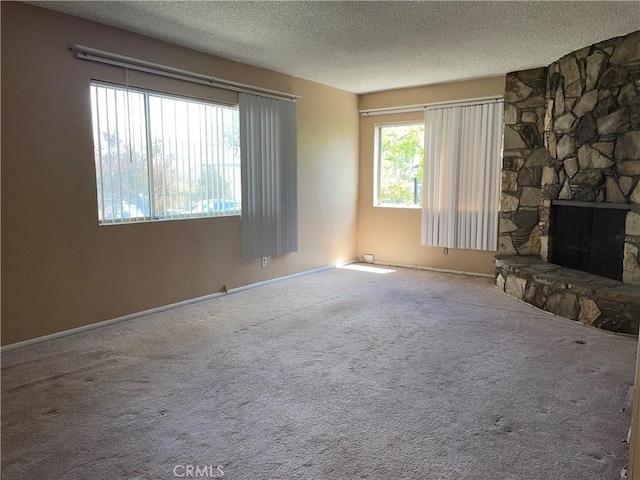 unfurnished living room featuring a fireplace, a textured ceiling, carpet flooring, and baseboards