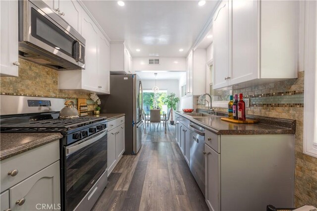 kitchen featuring stainless steel appliances, dark countertops, white cabinets, and a sink