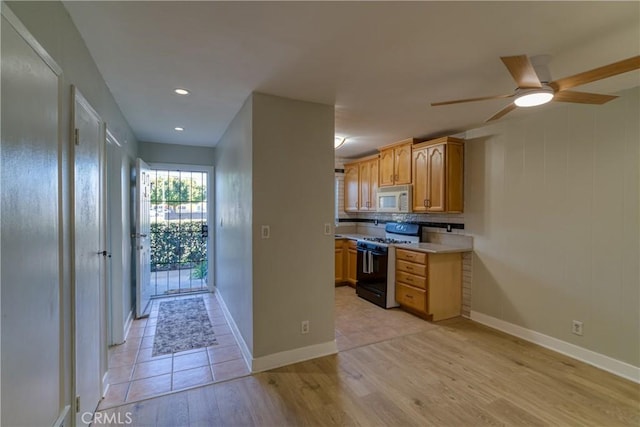 kitchen with black range with gas cooktop, white microwave, light wood-style flooring, baseboards, and light countertops