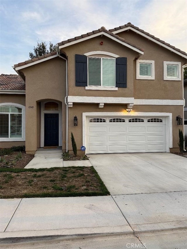 view of front of house with concrete driveway, an attached garage, a tiled roof, and stucco siding