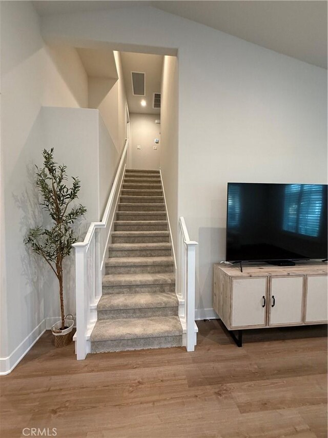 stairs featuring visible vents, vaulted ceiling, baseboards, and wood finished floors