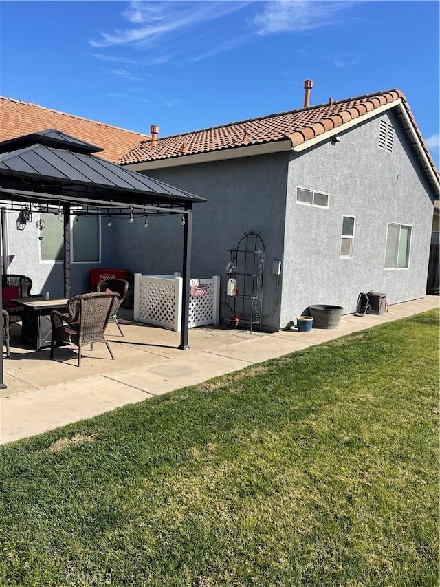 rear view of property with a lawn, a tiled roof, a gazebo, and stucco siding