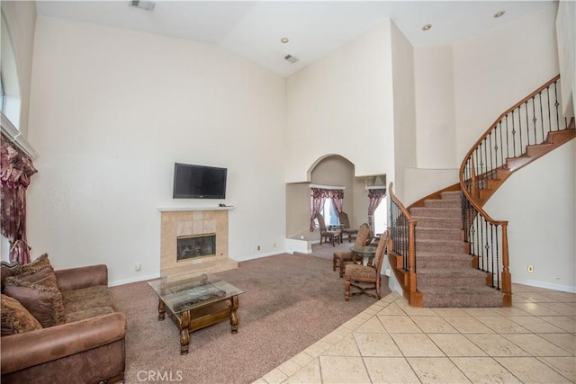 living area featuring stairs, high vaulted ceiling, a tiled fireplace, and light colored carpet