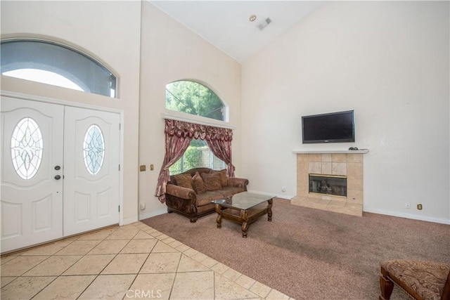 foyer entrance featuring light tile patterned floors, a tiled fireplace, light carpet, high vaulted ceiling, and baseboards