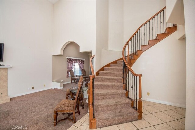 staircase with carpet floors, arched walkways, a high ceiling, tile patterned flooring, and baseboards