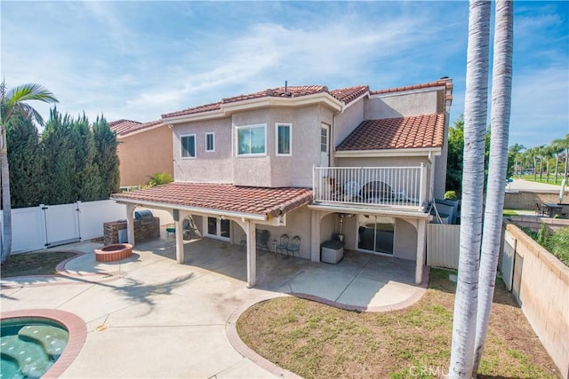 back of property with a tile roof, a fire pit, a balcony, and stucco siding