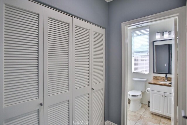 half bath with tile patterned flooring, toilet, vanity, baseboards, and a closet