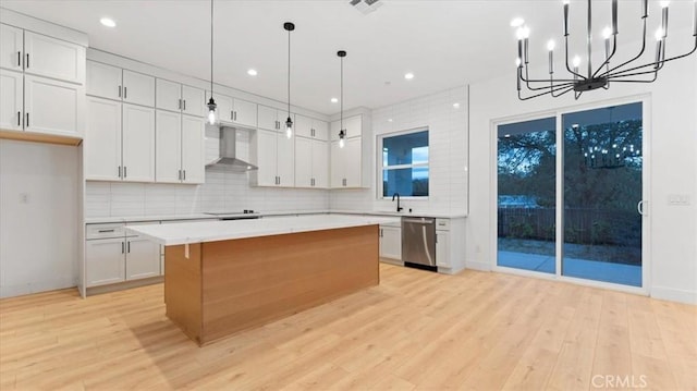 kitchen with white cabinets, hanging light fixtures, light countertops, dishwasher, and wall chimney exhaust hood