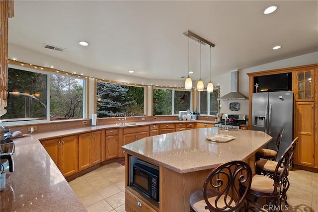 kitchen with stainless steel appliances, visible vents, hanging light fixtures, a sink, and wall chimney range hood