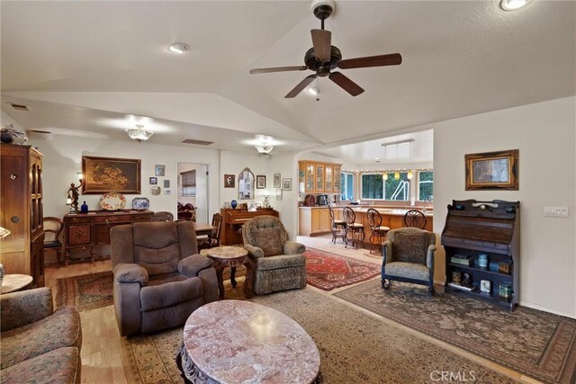 living room featuring lofted ceiling, visible vents, a ceiling fan, and light wood-style floors