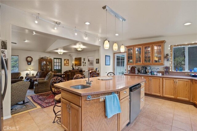 kitchen with a sink, open floor plan, light countertops, an island with sink, and glass insert cabinets