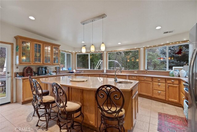 kitchen with light stone counters, a kitchen island with sink, a sink, visible vents, and hanging light fixtures