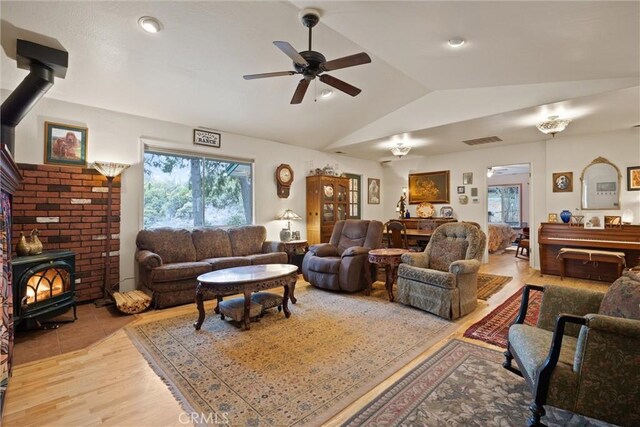 living area featuring light wood finished floors, visible vents, a ceiling fan, lofted ceiling, and a wood stove