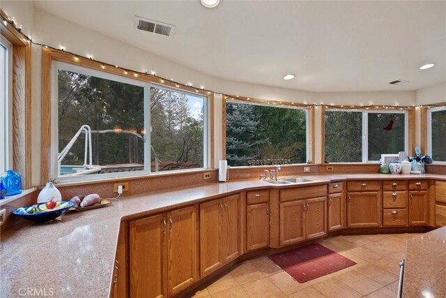 kitchen featuring light tile patterned floors, visible vents, brown cabinets, a sink, and recessed lighting