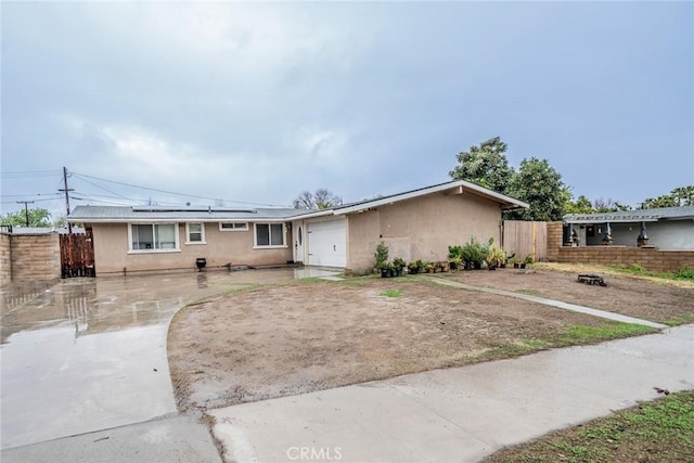 ranch-style house with driveway, solar panels, an attached garage, fence, and stucco siding