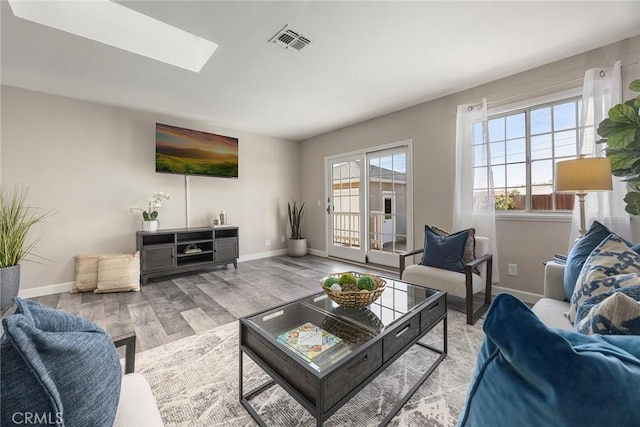 living room with a skylight, baseboards, visible vents, and light wood finished floors