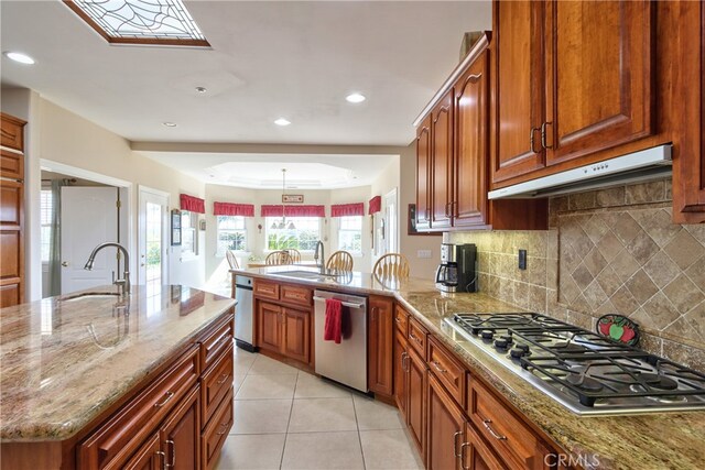 kitchen featuring appliances with stainless steel finishes, a sink, under cabinet range hood, and light stone counters