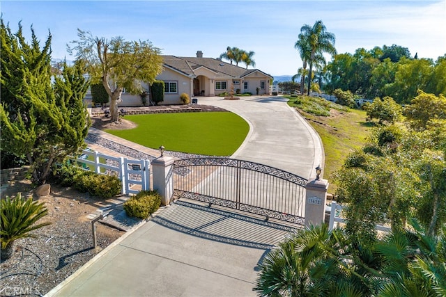 view of front of property featuring driveway, a gate, fence, and a front yard