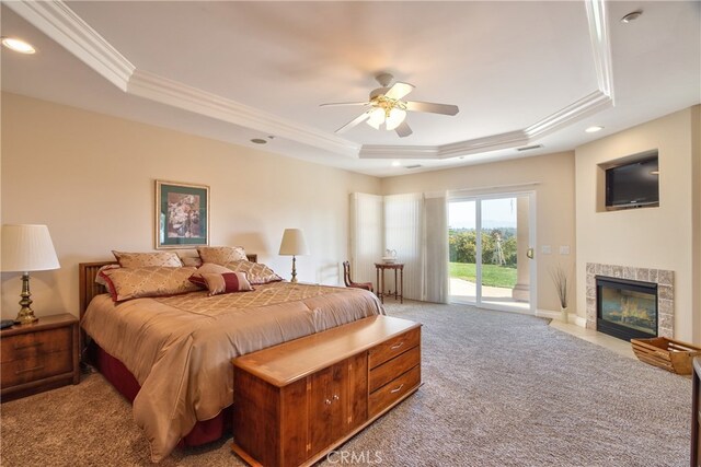 bedroom featuring a tiled fireplace, light colored carpet, access to outside, a tray ceiling, and crown molding