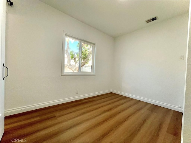 empty room with wood finished floors, visible vents, and baseboards