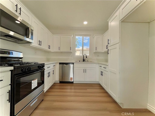 kitchen with appliances with stainless steel finishes, light countertops, a sink, and white cabinetry