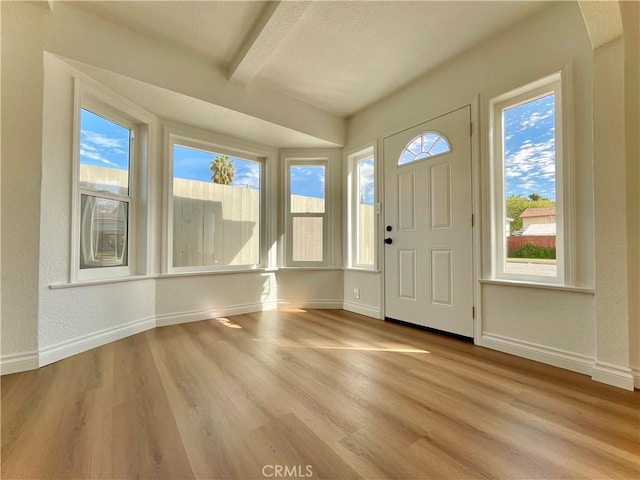 foyer entrance with a textured wall, baseboards, beamed ceiling, and light wood finished floors