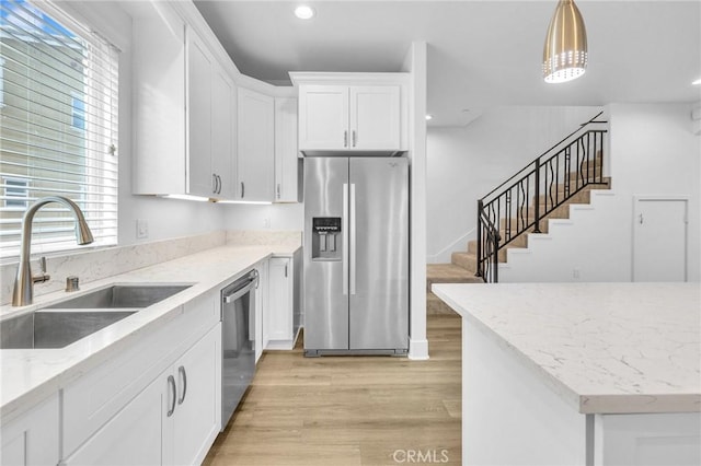 kitchen featuring decorative light fixtures, stainless steel appliances, light wood-style flooring, white cabinetry, and a sink