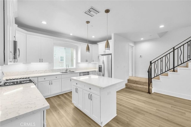 kitchen with visible vents, appliances with stainless steel finishes, white cabinets, a kitchen island, and a sink