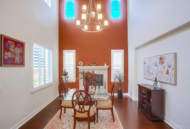 dining space featuring dark wood-style floors, a towering ceiling, baseboards, and an inviting chandelier