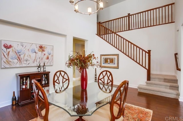 dining room featuring a notable chandelier, dark wood finished floors, stairway, a high ceiling, and baseboards