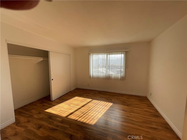 unfurnished bedroom featuring a closet, dark wood finished floors, and baseboards