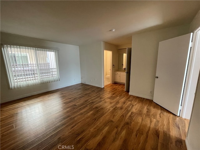 unfurnished bedroom with ensuite bathroom, wood finished floors, and baseboards