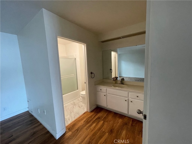 bathroom with shower / bathtub combination, toilet, vanity, wood finished floors, and baseboards